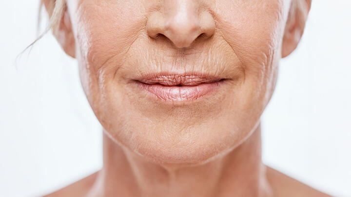 Closeup of an elderly woman with wrinkles, light pink lip gloss on her lips