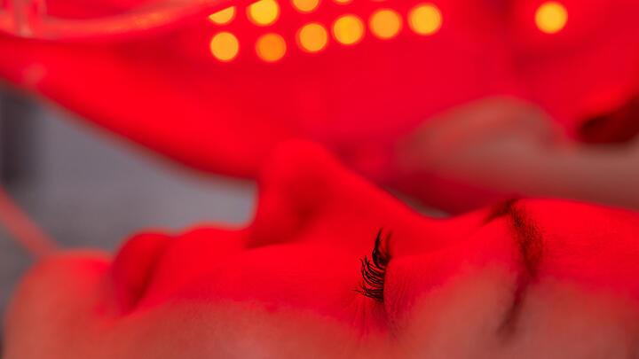 A closeup of a young woman's face sideways. She is lying down, content, with her eyes closed under red LED light therapy